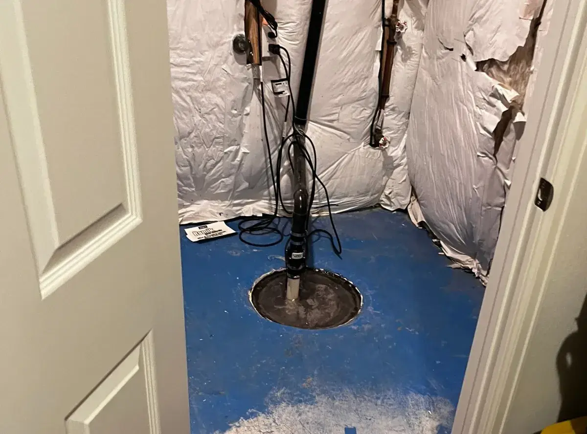Sump pump basin in basement utility closet with blue vapor barrier flooring