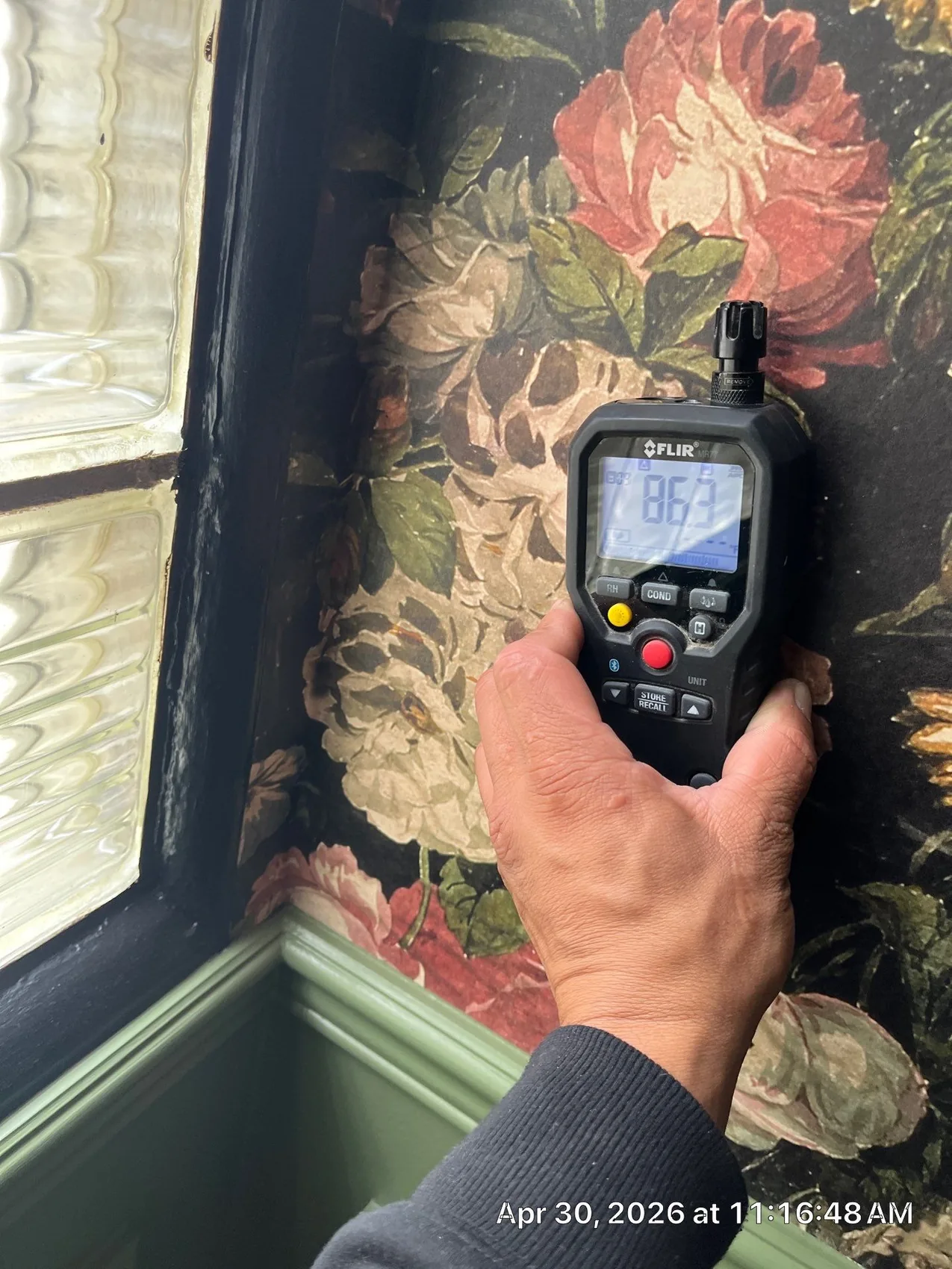 A moisture meter reading high moisture in a wall that looks dry
