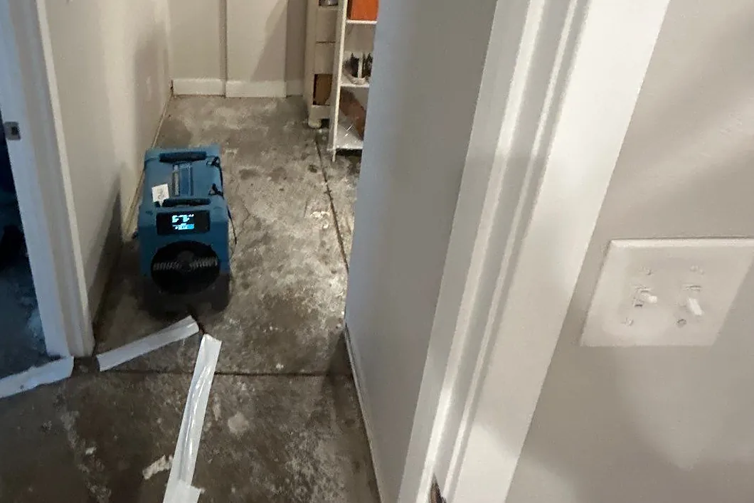 Blue air mover drying an exposed concrete subfloor after sewage cleanup