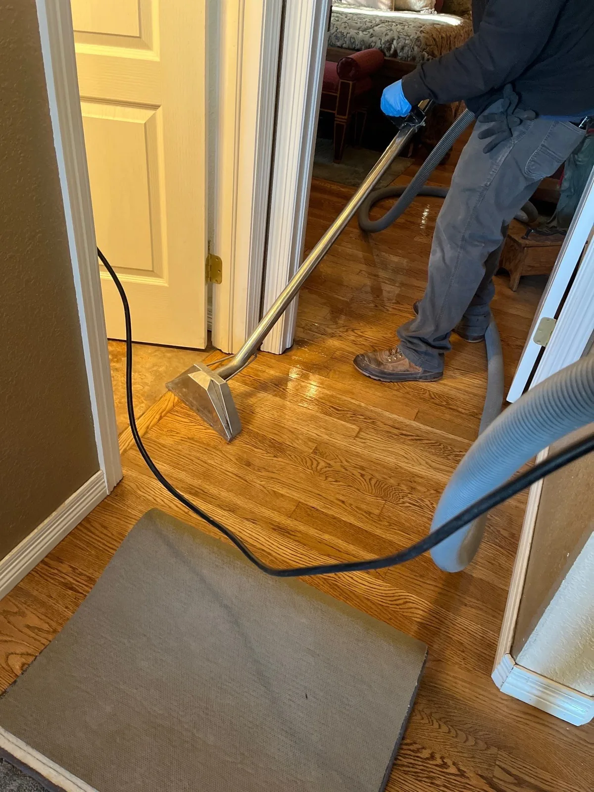 A technician extracting contaminated water from a hardwood floor with an extraction wand