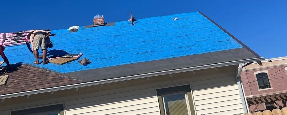 Roofing crew installing synthetic underlayment after storm and hail damage