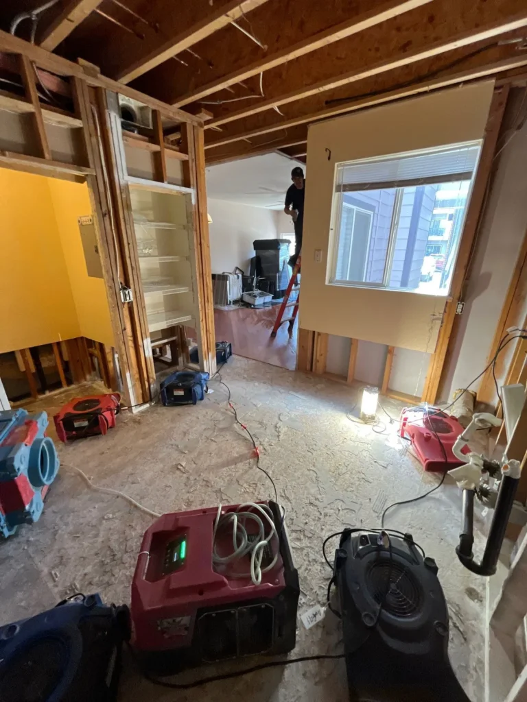 Drying equipment running as a technician works in a wall-out space during water damage mitigation