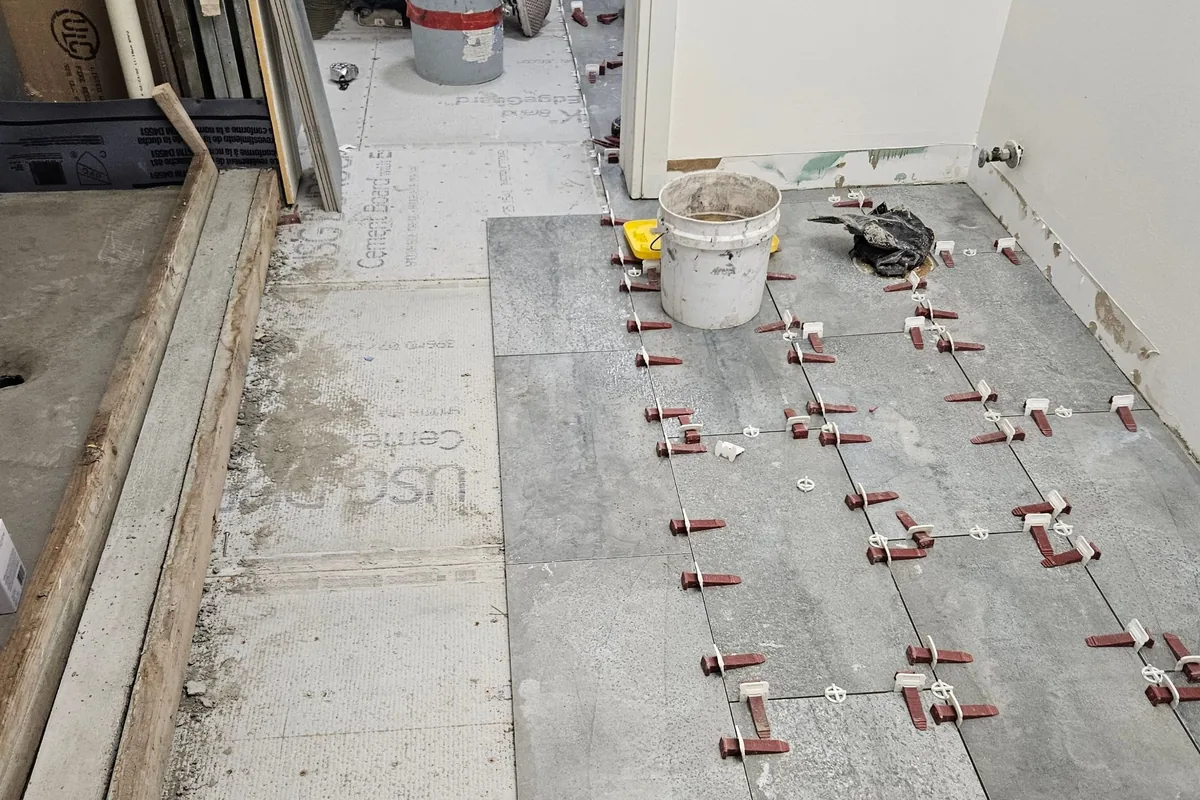New floor tile being installed with leveling clips during a sewage-damage rebuild