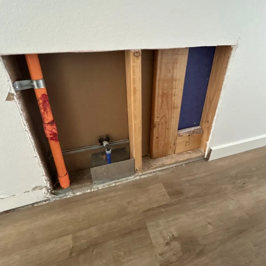 Drywall opened at the base of a wall exposing the plumbing and wall framing